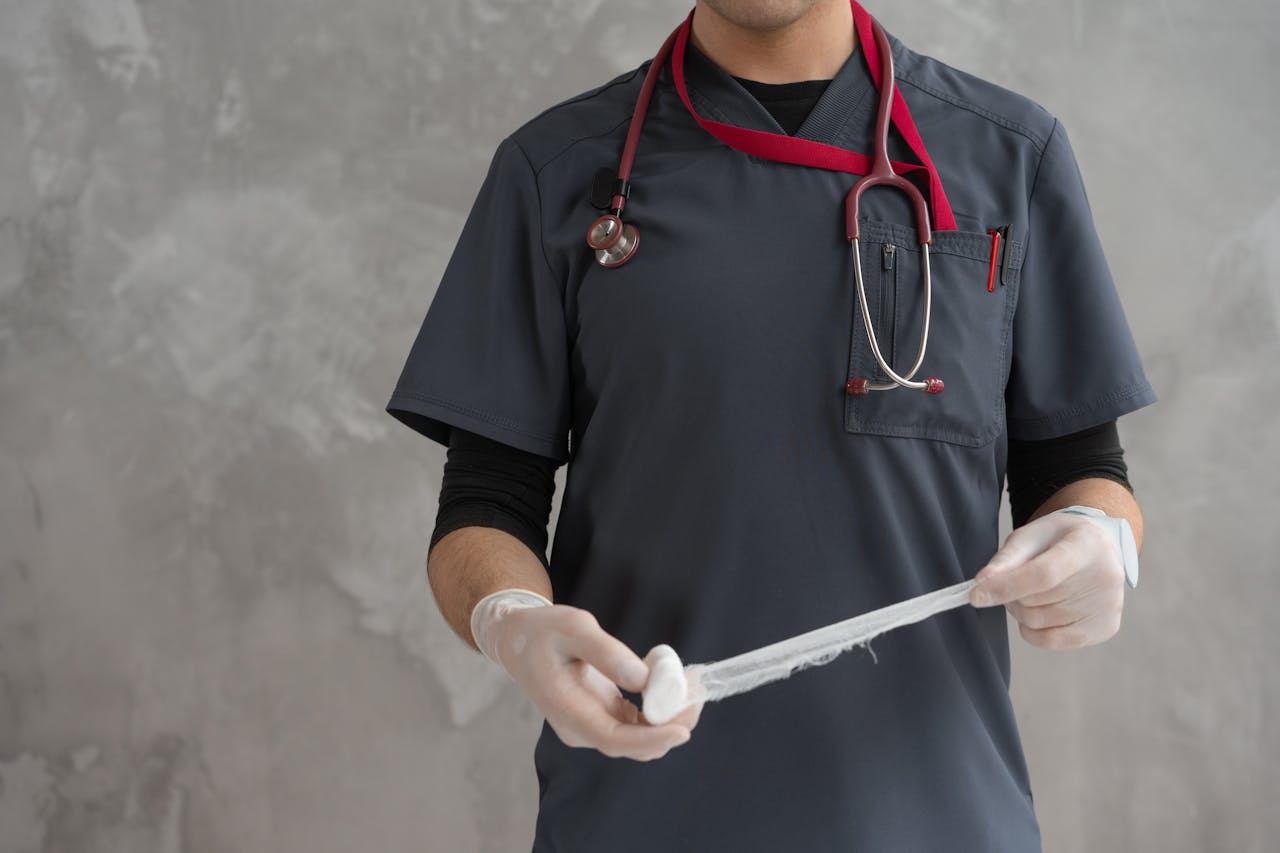 Healthcare worker preparing gauze bandage wearing stethoscope and gloves.